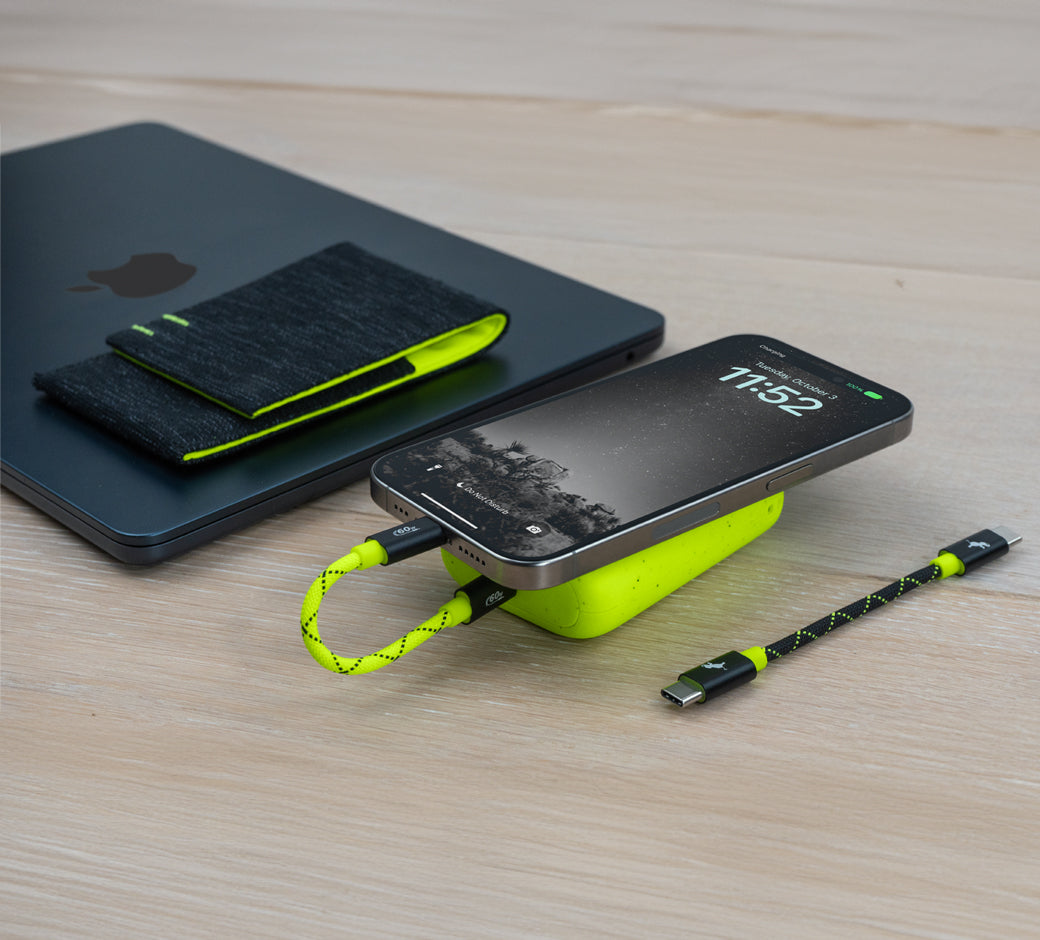 Power bank and cables charging a phone near a laptop.