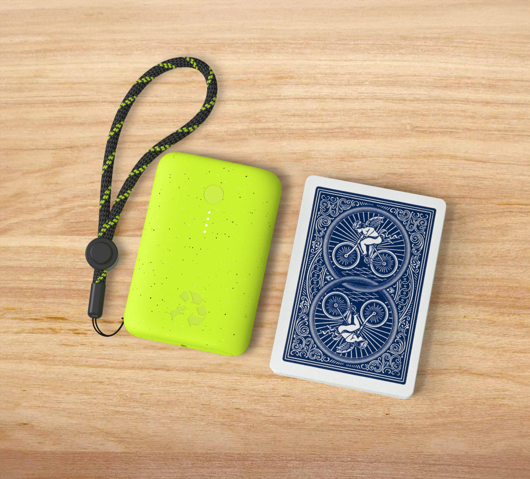 Neon green power bank with a black strap beside playing cards on wood.